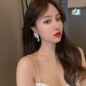 Elegant white floral earrings with crystal droplets worn by a model in a warm setting