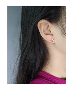 Detailed view of a woman wearing gold-toned S925 sterling silver heart knot stud earrings