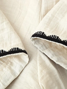 Detail of off-white linen fabric featuring black geometric embroidery and textured weave