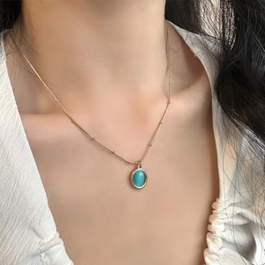 Elegant gold titanium necklace featuring a blue cat-eye stone pendant on model