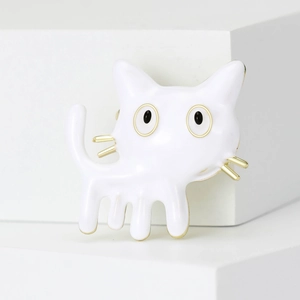 Close-up of white enamel cartoon cat brooch with gold edges on white geometric block