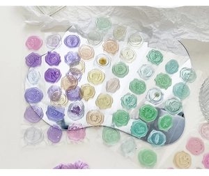 Flat lay of colorful semi-transparent floral wax seal stickers on white textured paper