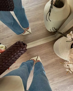 Nahaufnahme von cremefarbenen Pumps mit blauen Fransen-Jeans und gewebter brauner Clutch