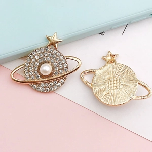 Golden Saturn-shaped alloy charm with white rhinestones and a central pearl accent