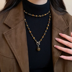 Dettaglio della collana di perle occhio di tigre con chiusura OT su giacca di pelle