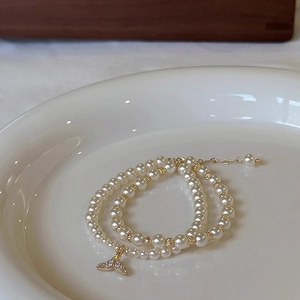 Macro shot of layered pearl bracelet with a gold fishtail charm and zircon inlay
