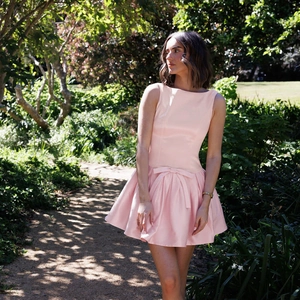 Detailed view of pink satin sleeveless dress featuring waist bow and pleated A-line skirt