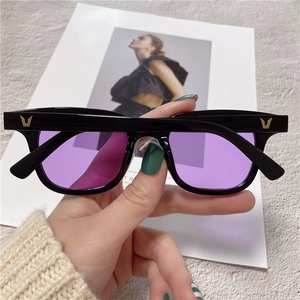 Detailed macro view of purple lenses and black square frame with metal V-shaped logo