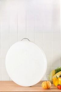 Solid white PE plastic round cutting board with metal handle on a wooden tabletop