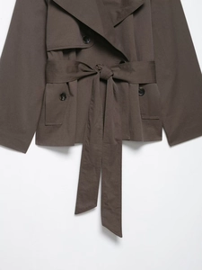 Detail eines kurzen braunen Trenchcoats mit zweireihigen Knöpfen und Taillengürtel