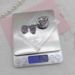 Detailed view of purple strawberry keychain on a scale weighing 14.2g with silver ring