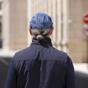 Back view of a blue washed denim beret paired with a dark blue casual vest in a city setting