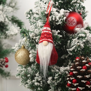 Charming faceless gnome ornament with red knitted hat hanging on a snowy Christmas tree