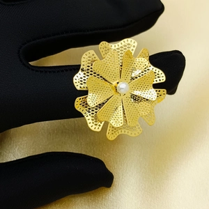 Detailed close-up of hollow gold flower ring with center pearl on black velvet glove