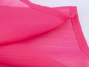 Détail du tissu en mousseline rose vif avec texture verticale et couture d'ourlet fine