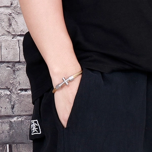 Detail of twisted steel wire bracelet with cross charm on wrist in streetwear style