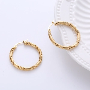 Macro shot of 30mm golden twisted spiral hoop earrings on a minimalist white ceramic plate