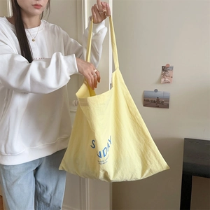 Detail of light yellow canvas tote bag featuring blue Sunday Summer Night lettering