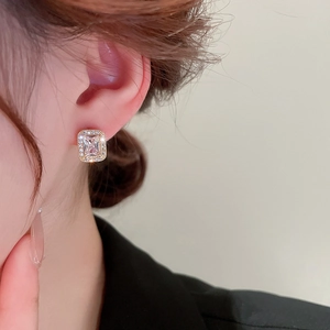 Close-up of golden square zircon stud earrings worn by a model in soft lighting