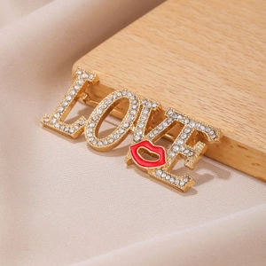 Broche LOVE dorée ornée de strass et d'une lèvre rouge sur un support en bois