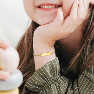 Polished gold rectangular nameplate on a child's stainless steel bracelet with a thin chain