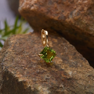 Macro shot of a square green gemstone pendant in gold setting on a natural rock surface