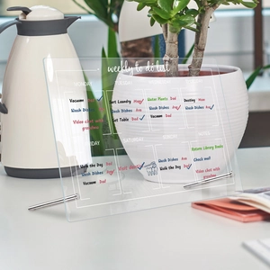 Detail of clear acrylic weekly planner with metal stand showing to-do lists on a desk