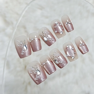 Pink cat eye press-on nails with 3D pearls and rhinestones on white faux fur background