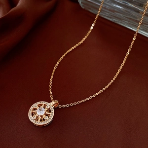 Detailed shot of a gold-plated circular compass pendant necklace with zircon on brown silk