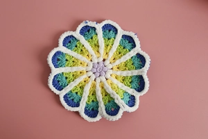 Macro shot of handmade crochet coaster with colorful floral petals on a pink background