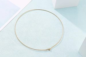 Flat lay of golden snake chain necklace with lobster clasp on light blue background