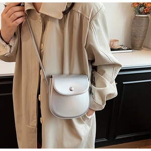 Detailansicht einer silbernen Mini-Satteltasche mit rundem Druckknopf auf Khaki-Mantel