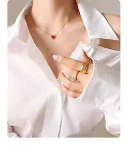 Detail of red heart pendant necklace in 18k gold plating worn with gold rings