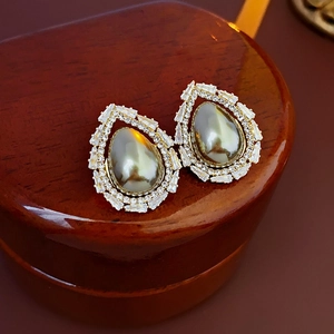 Close-up of golden teardrop earrings with grey pearl center and sparkling zircon stones