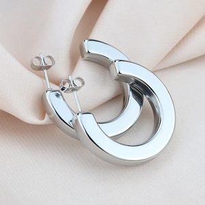 Macro shot of silver C-shaped chunky hoop earrings on elegant silk fabric background