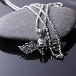 Silver stainless steel skull with wings pendant on a snake chain over dark stone