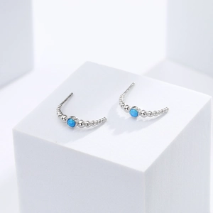Detailed view of silver arc earrings with round blue opal stones on a white stand