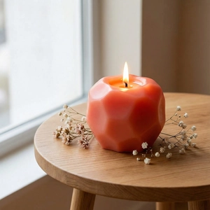 Close-up of lit orange geometric apple scented candle on a rustic wooden stool