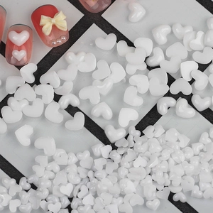 Primer plano de dijes de resina blanca en forma de corazón con ejemplos de manicura
