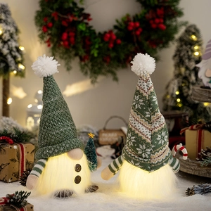 Close-up of glowing plush Christmas gnomes with knit hats holding tree and candy cane