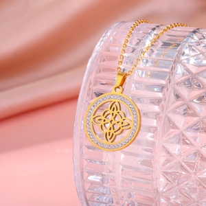 Détail du pendentif nœud de sorcière doré avec zircons sur fond en soie rose