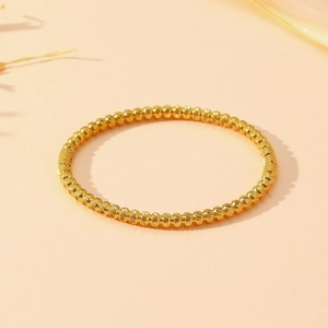 Detailed view of a gold beaded bangle with high-shine metallic finish on a beige background