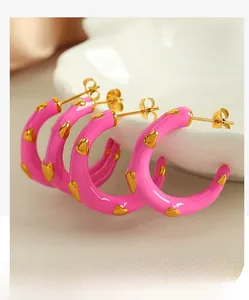 Macro detail of pink enamel C-shaped earrings with gold heart patterns on a ceramic dish