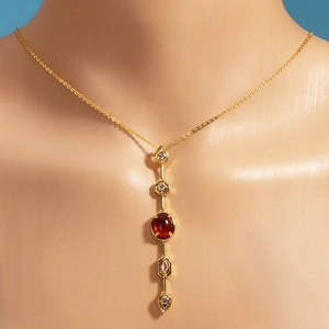 Detailed view of 18K gold plated necklace with red and clear gemstones on a mannequin