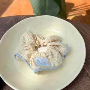 Detailed shot of beige checkered scrunchie with blue piping and creative label in a ceramic bowl