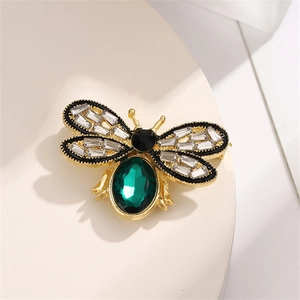 Macro detail of bee brooch featuring a large green faceted stone and crystal wings