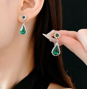 Detail of vintage silver earrings with green pear-shaped stones and floral studs