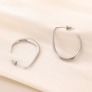 Close-up of silver U-shaped curved earrings on textured beige fabric background