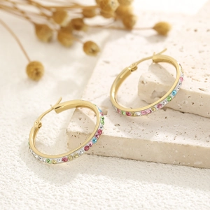Macro shot of gold hoop earrings with colorful crystals on a textured stone surface