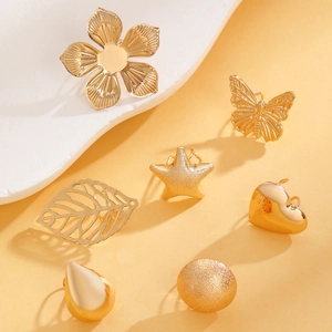 Detail view of gold-tone star and butterfly ear clips on a white stone background